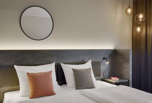 Hotelzimmer mit Doppelbett, runden Kissen und Wandlampe.
